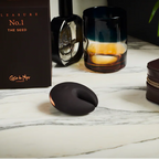 Brown silicon object, glass with candle, and brown leather case on a marble surface.