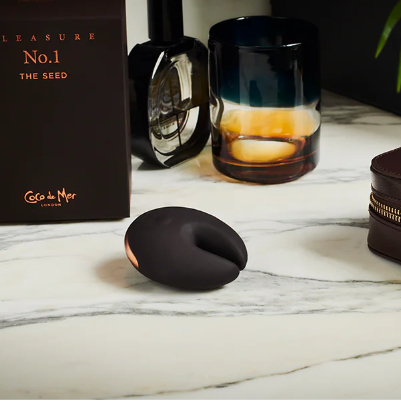 Brown silicon object, glass with candle, and brown leather case on a marble surface.